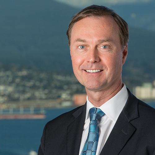 Smiling man in suit and tie with coastal city in the background.